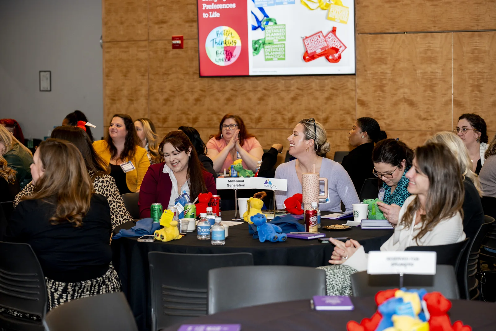 Women seated at tables during the Women in Thought Summit with participant materials and presentation content visible.
