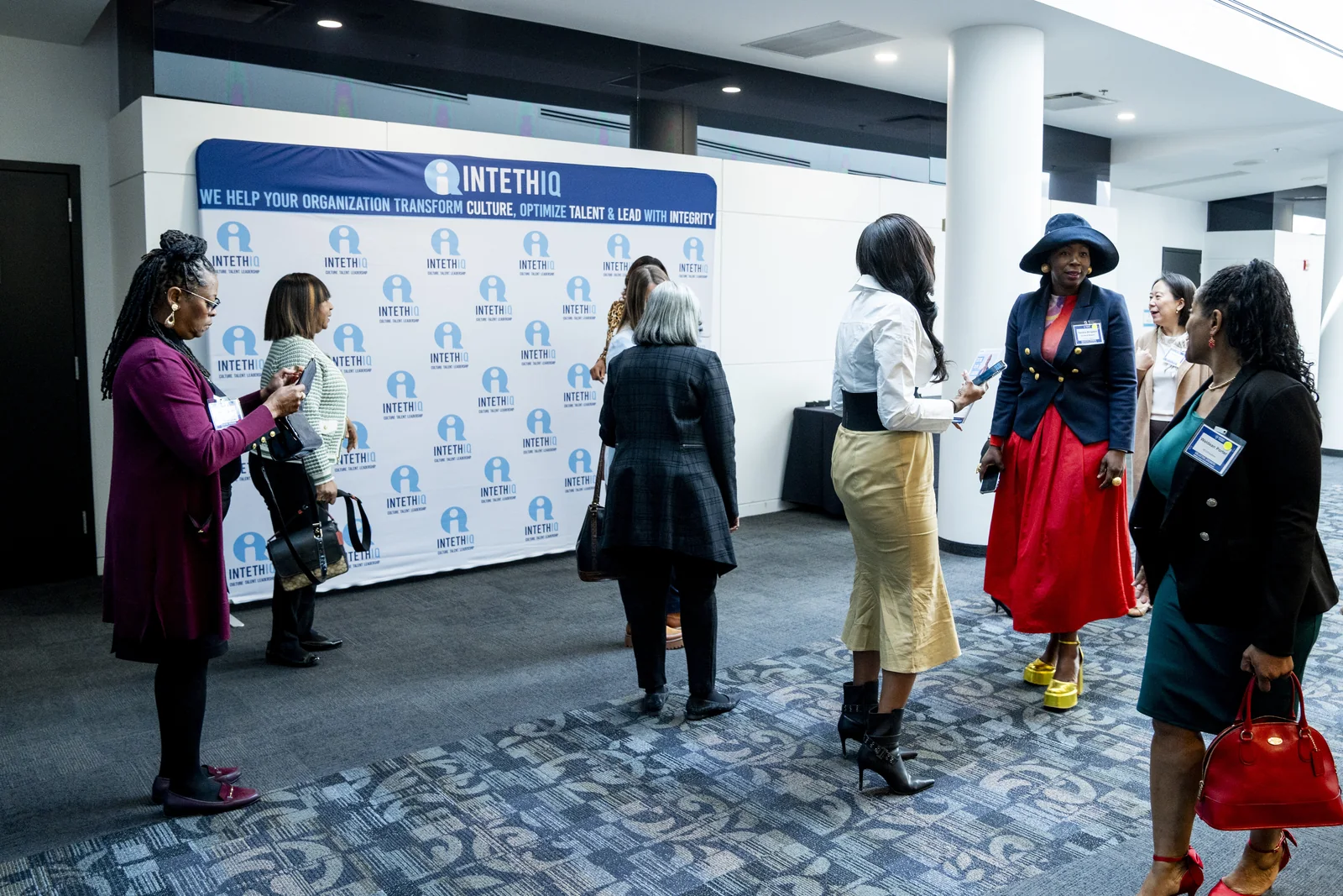 Participants gathering and talking near Women in Thought Summit arrival and step-and-repeat signage.